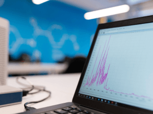 Laptop with data graphs on screen on a desk in a modern office, with blurred blue background indicating a corporate or tech environment.