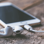 Smartphone with earbuds on a wooden surface.