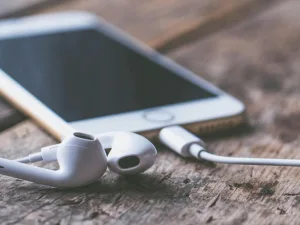 Smartphone with earbuds on a wooden surface.