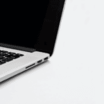 Partial view of an open laptop with a black keyboard on a white background, showing USB and audio ports on its side.