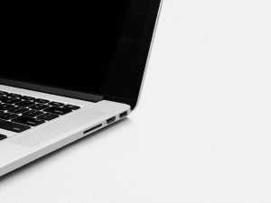 Partial view of an open laptop with a black keyboard on a white background, showing USB and audio ports on its side.