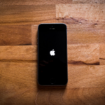 Alt text: A black iPhone with a lit Apple logo centered on a wooden parquet surface.