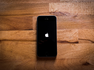 Alt text: A black iPhone with a lit Apple logo centered on a wooden parquet surface.