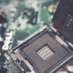 Close-up of an open CPU socket on a motherboard with electronic components and capacitors in the background.