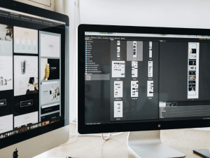 Two computer monitors on a desk displaying a website design project and a folder structure in a professional workspace.