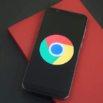 Smartphone lying on a red notebook with the Google Chrome logo displayed on the screen, set on a dual-tone black and red background.