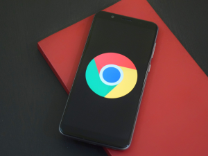 Smartphone lying on a red notebook with the Google Chrome logo displayed on the screen, set on a dual-tone black and red background.