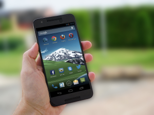 Hand holding a smartphone with a mountain wallpaper on screen, blurred background of a residential area.