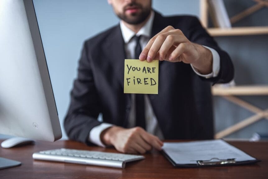man holding up a stick-it note that says "you are fired"